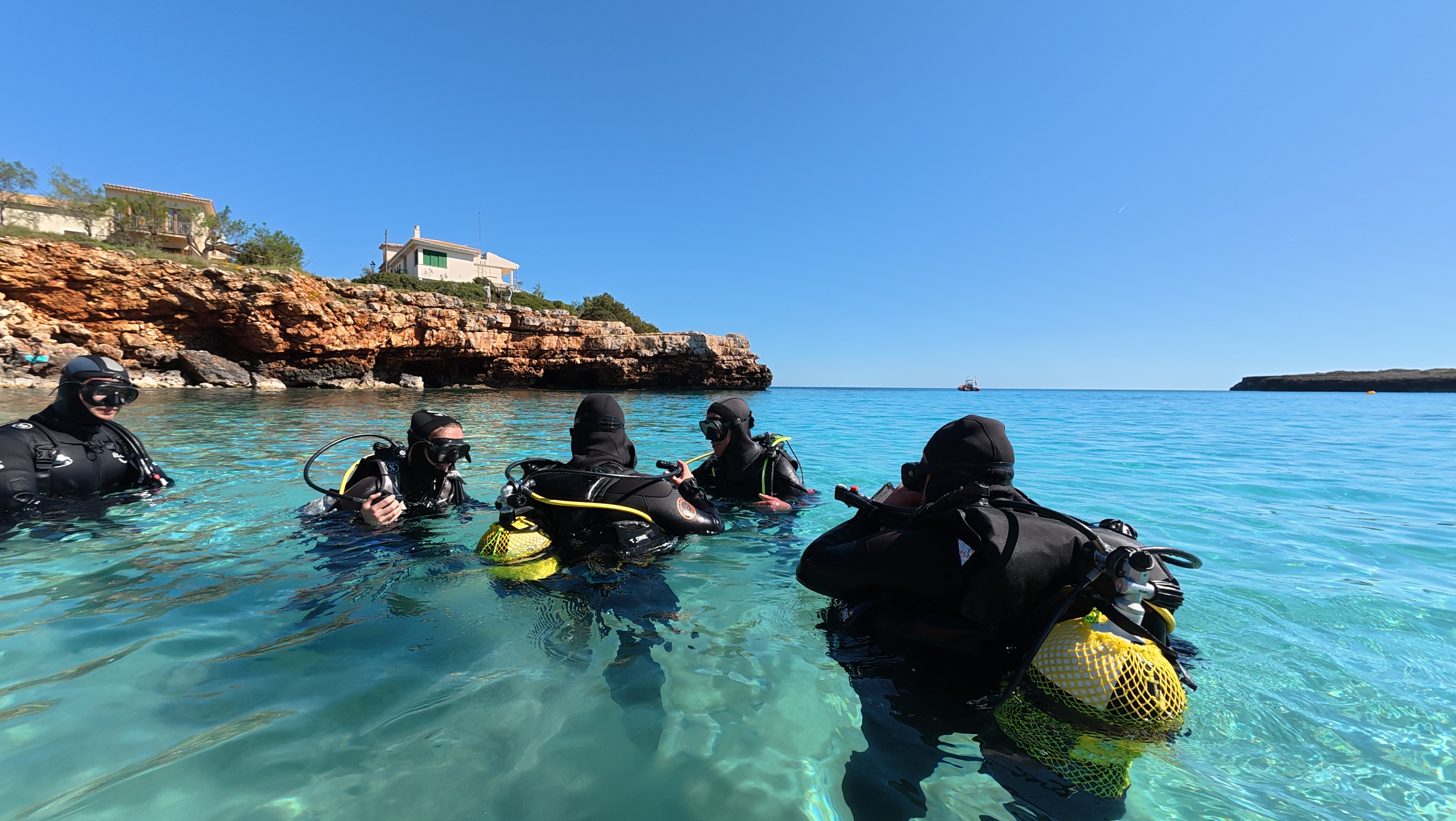 Aerial view of scuba divers in clear turquoise water along Mallorca's rocky east coast