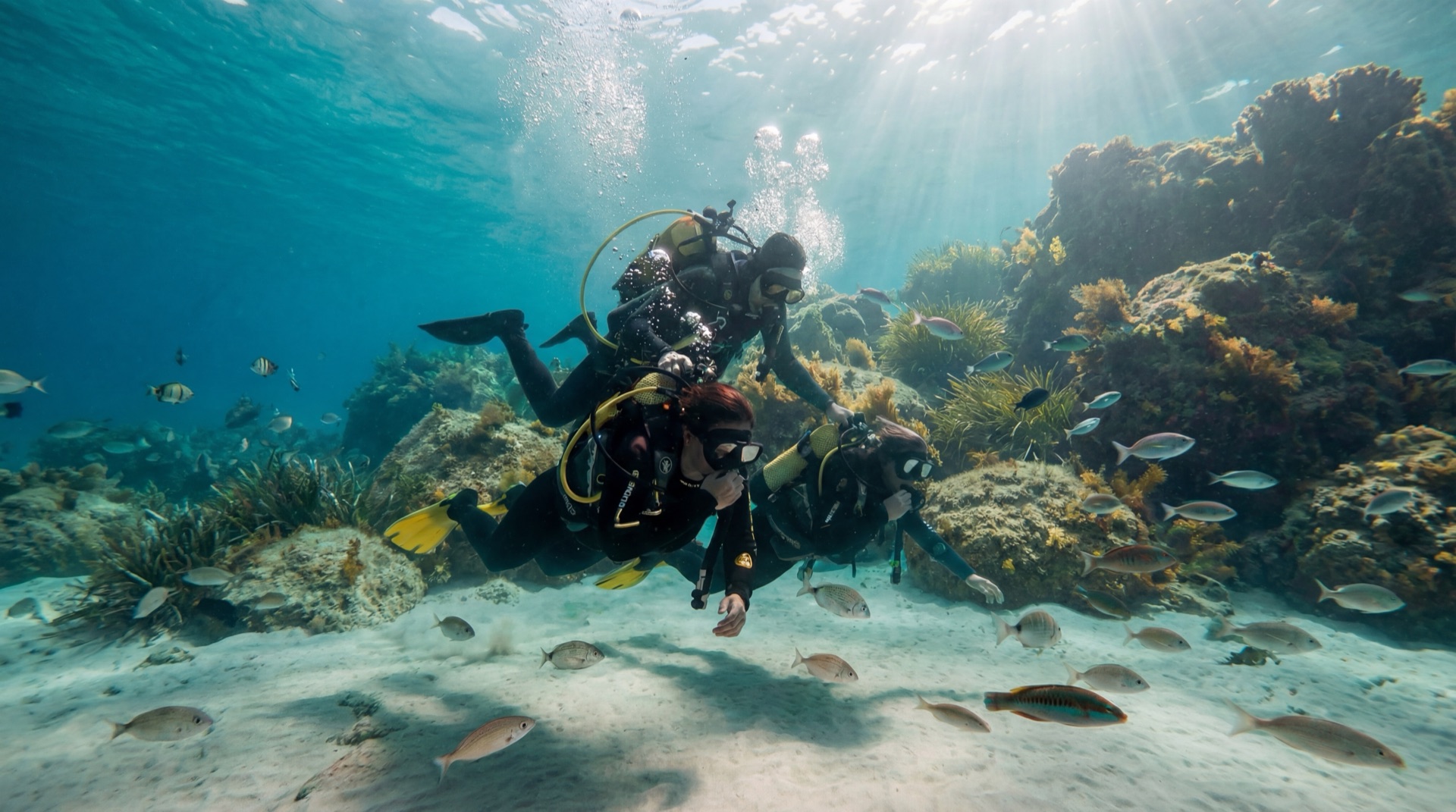 Two certified divers exploring a rocky reef in clear Mediterranean water